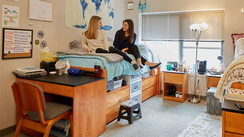 Two students smiling while seated in a double occupancy bedroom at the Living and Learning Commons ELS student residence at Saint Joseph's University in Philadelphia, Pennsylvania, USA.