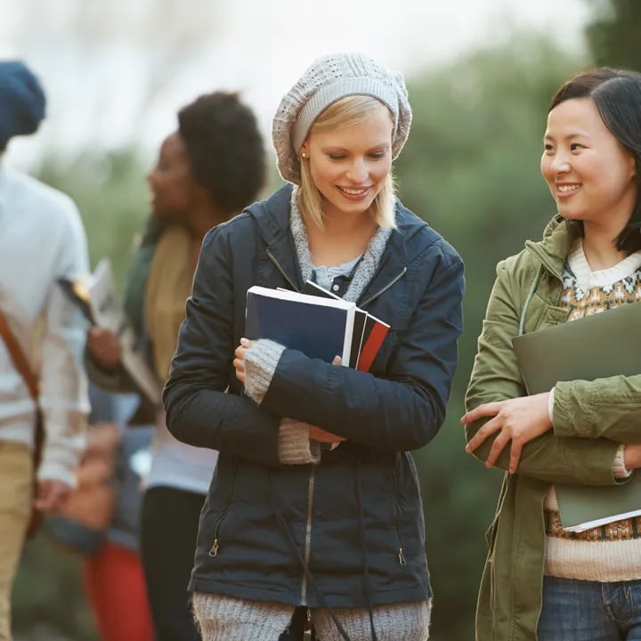 Female English student carrying books and walking with peers on a university campus in the USA