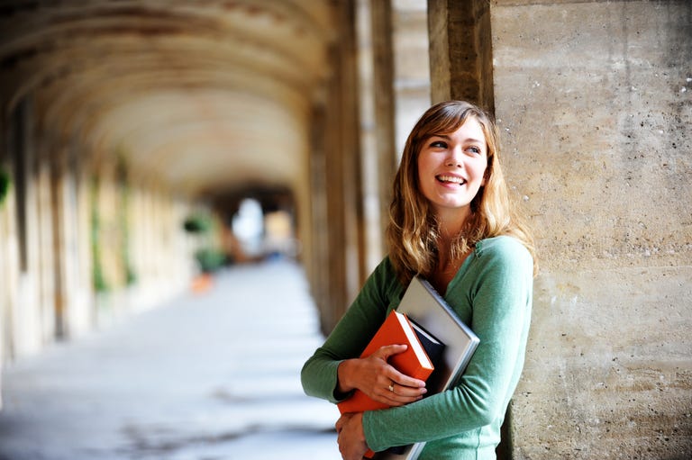 A female English language student holding books and smiling while outdoors on a university campus in the USA