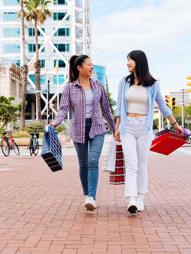 Two people walking together while holding shopping bags. Visitors can enjoy shopping trips at Melbourne Downtown Pedestrian Mall in Florida, USA near ELS Language Centers.