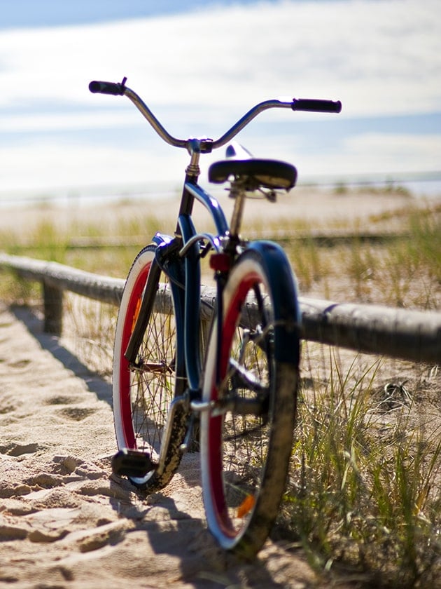 A bicycle parked along a sandy trail leading to the ocean.