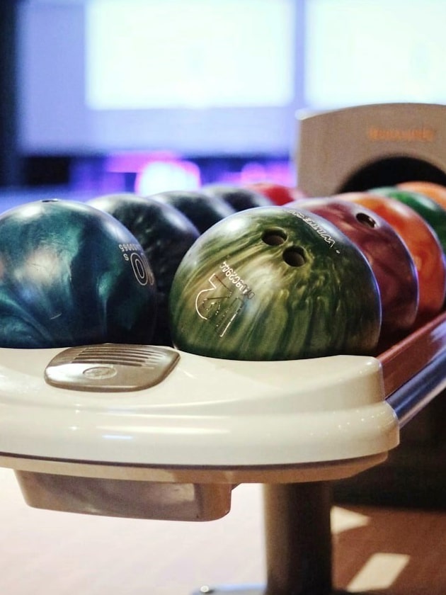 Colorful bowling balls lined up along a bowling ball return device inside a bowling alley, one of the many recreational spots you can visit in St. Petersburg, Florida, USA, near ELS Language Centers. 